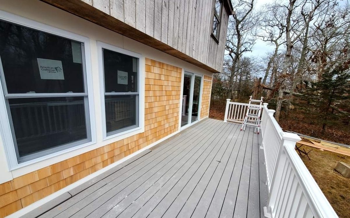 A gray composite deck with white rail beside new cedar shingle siding