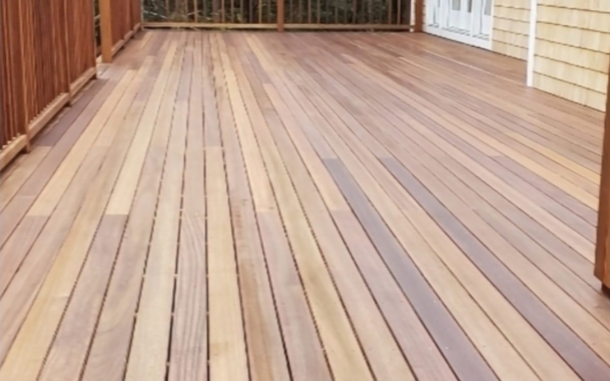 Wide hardwood deck boards running out to a rail and a shingled house