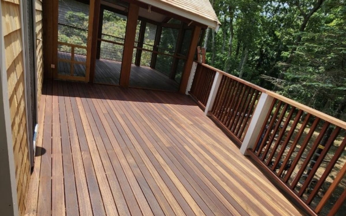 A mahogany deck running along a shingled house out to a screened porch