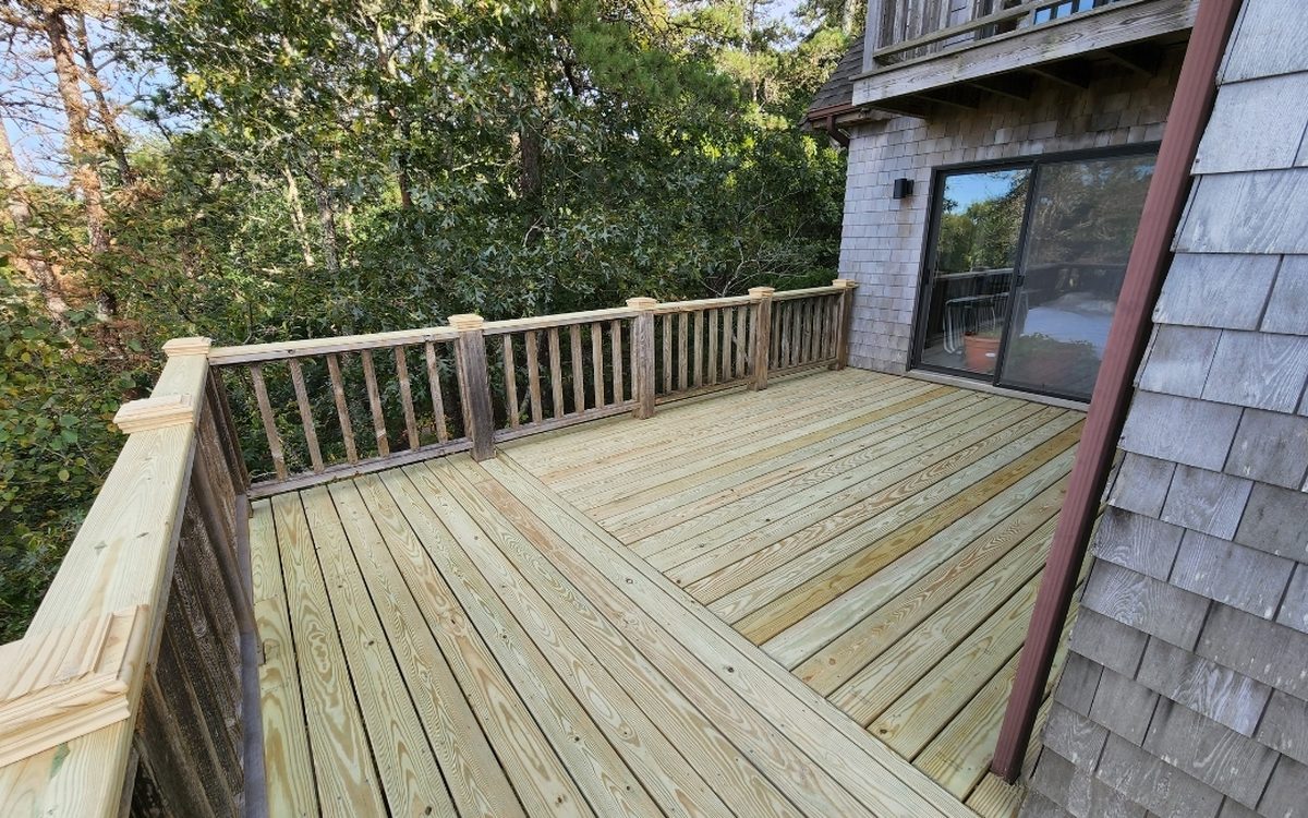 A pressure-treated deck meeting the shingled wall and slider of a house