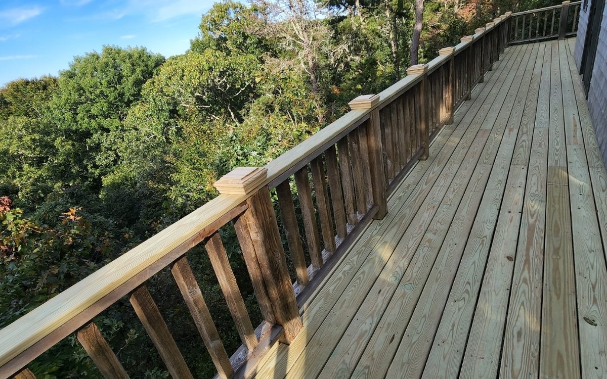 A long pressure-treated deck walkway running along a shingled house