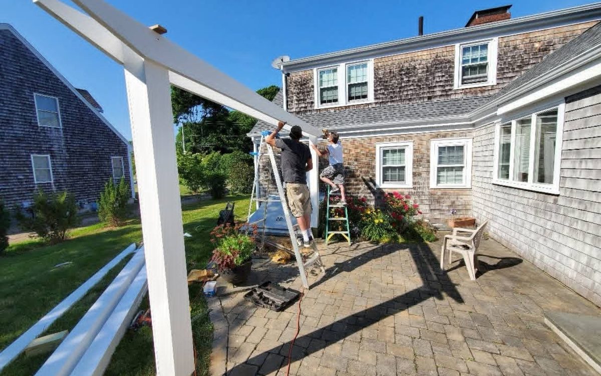Two Green Island Homes carpenters setting a pergola beam from ladders
