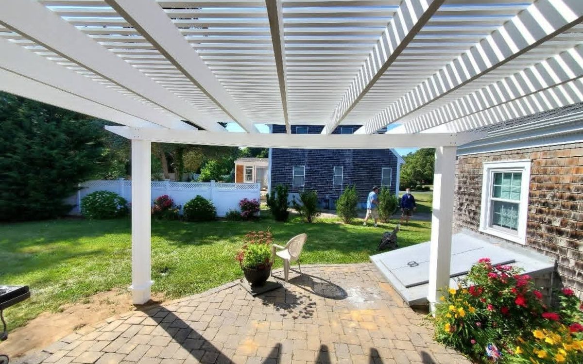 A white open-slat pergola shading a brick paver patio
