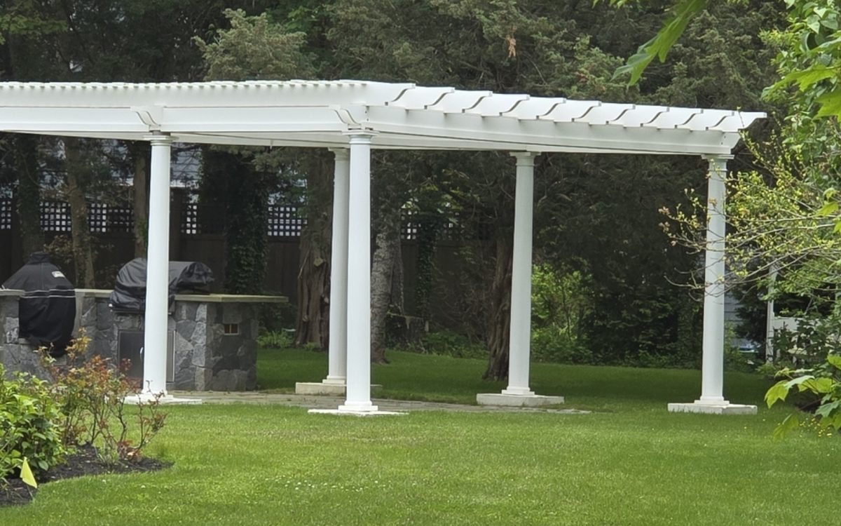 A white pergola over a stone grill station beside a lawn