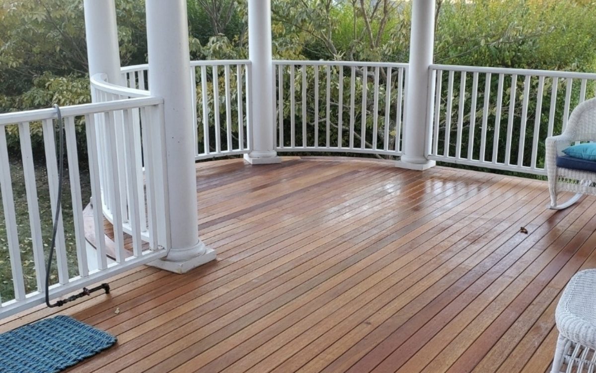 A hardwood porch floor under white turned columns and a curved white rail