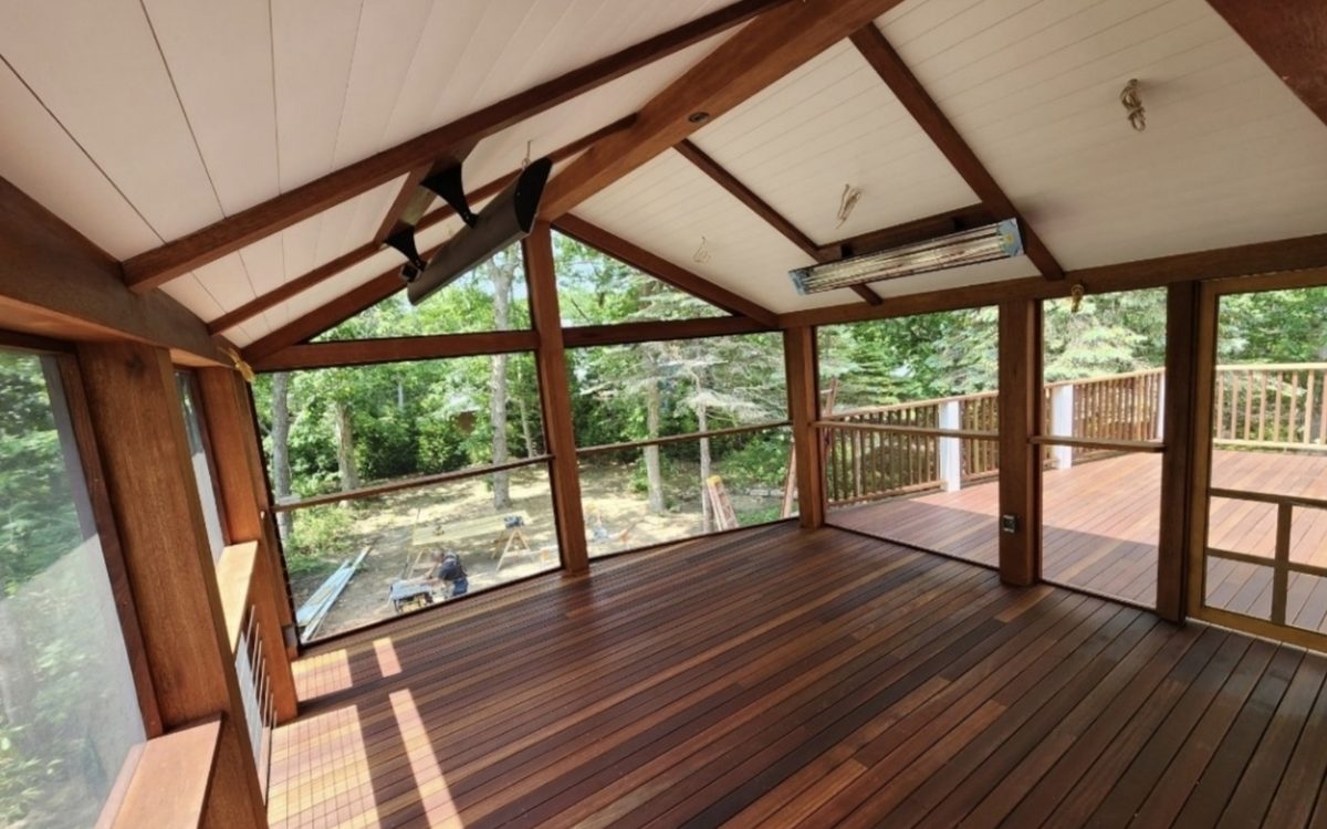 Inside a screened porch with a timber frame, hardwood floor and vaulted board ceiling